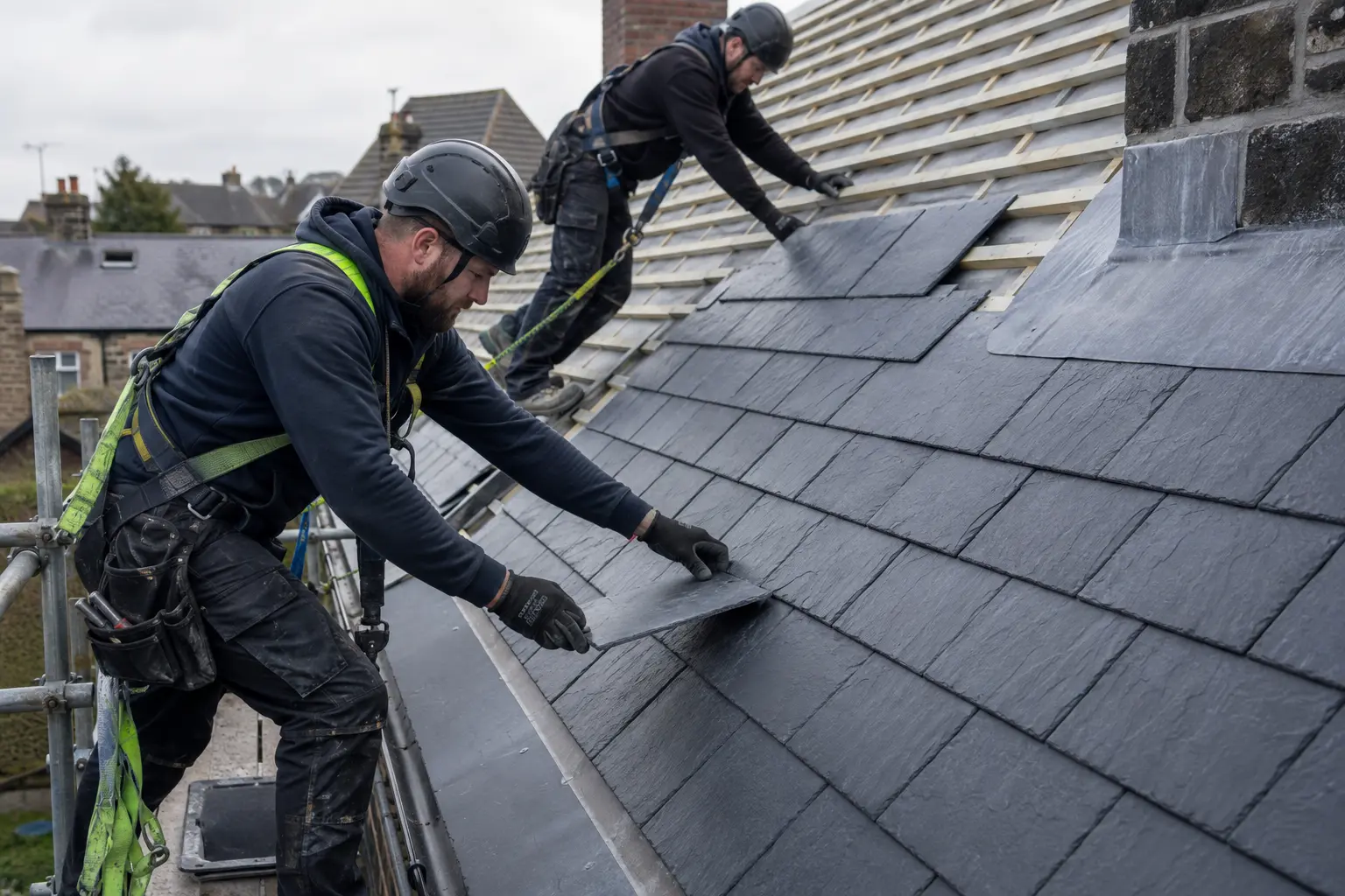 Roofers installing dark slate on a pitched UK house roof